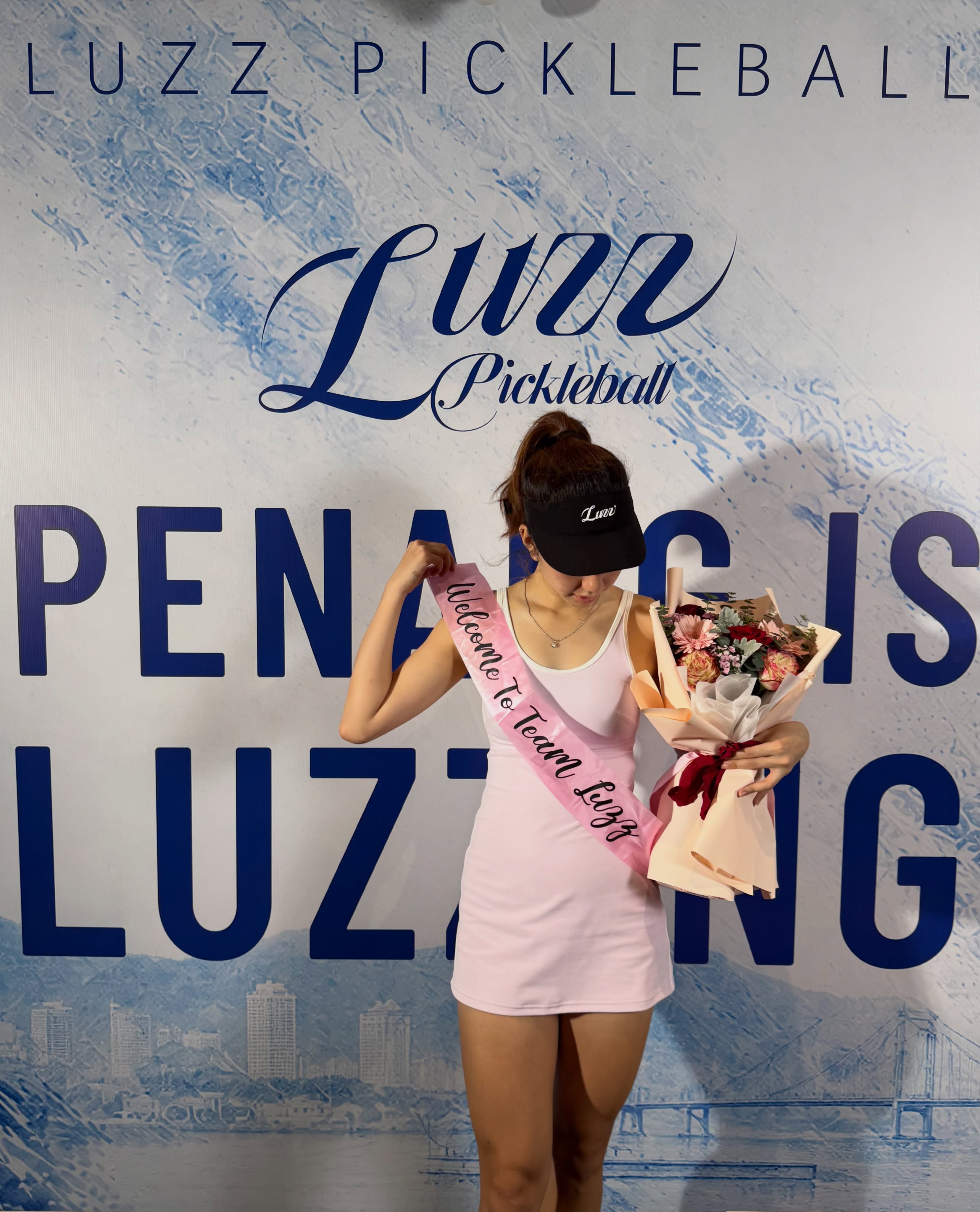 Sabrina Gee wearing a Welcome to Team Luzz sash in front of a Penang is Luzzing backdrop for Luzz Pickleball