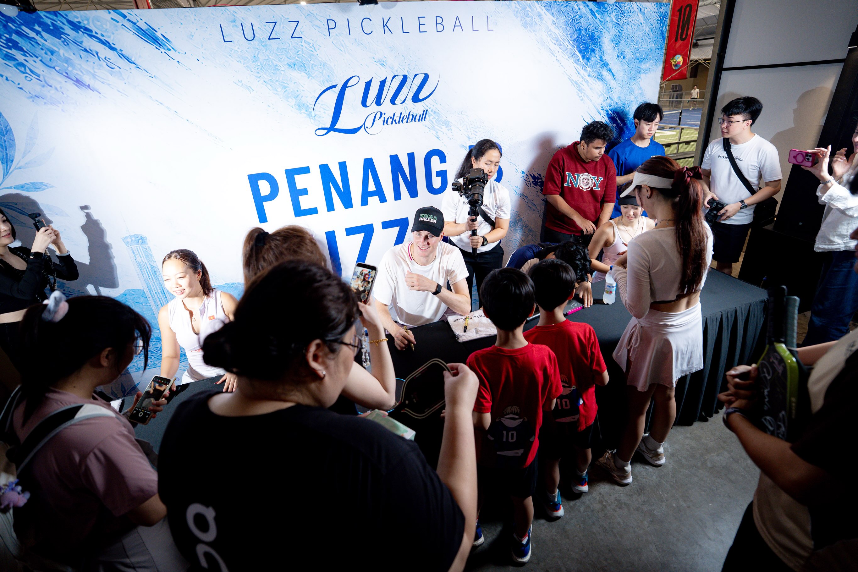 Sophia Tran Phuong Anh signs autographs for fans in front of the Luzz Pickleball Penang backdrop.