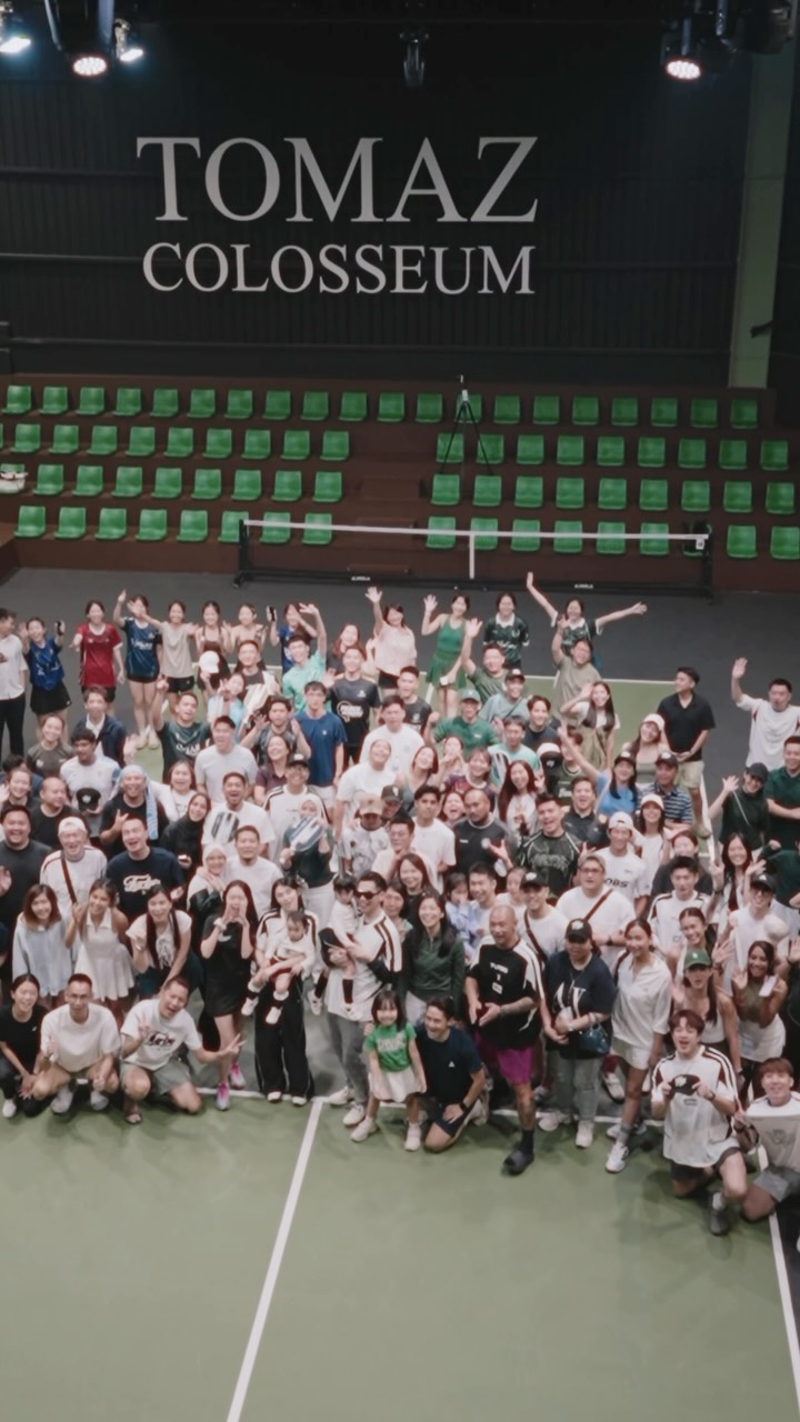 A crowd of players and guests on the court beneath the Tomaz Colosseum sign at Tomaz Pickleball Club