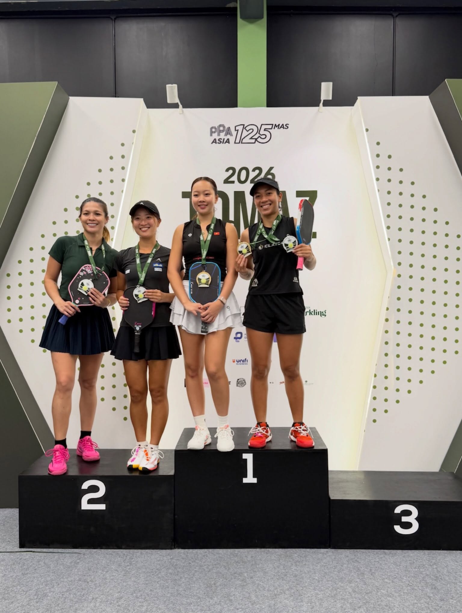 Sophia Tran and Tya Karina stand together on the number 1 podium alongside the tournament's other Women's Doubles Pro medalists.
