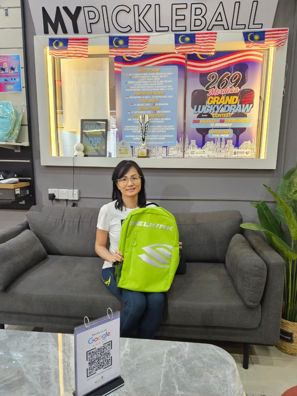 A winning MyPickleball customer poses with a Selkirk backpack in front of the Merdeka sale posters at the Strand Mall outlet.