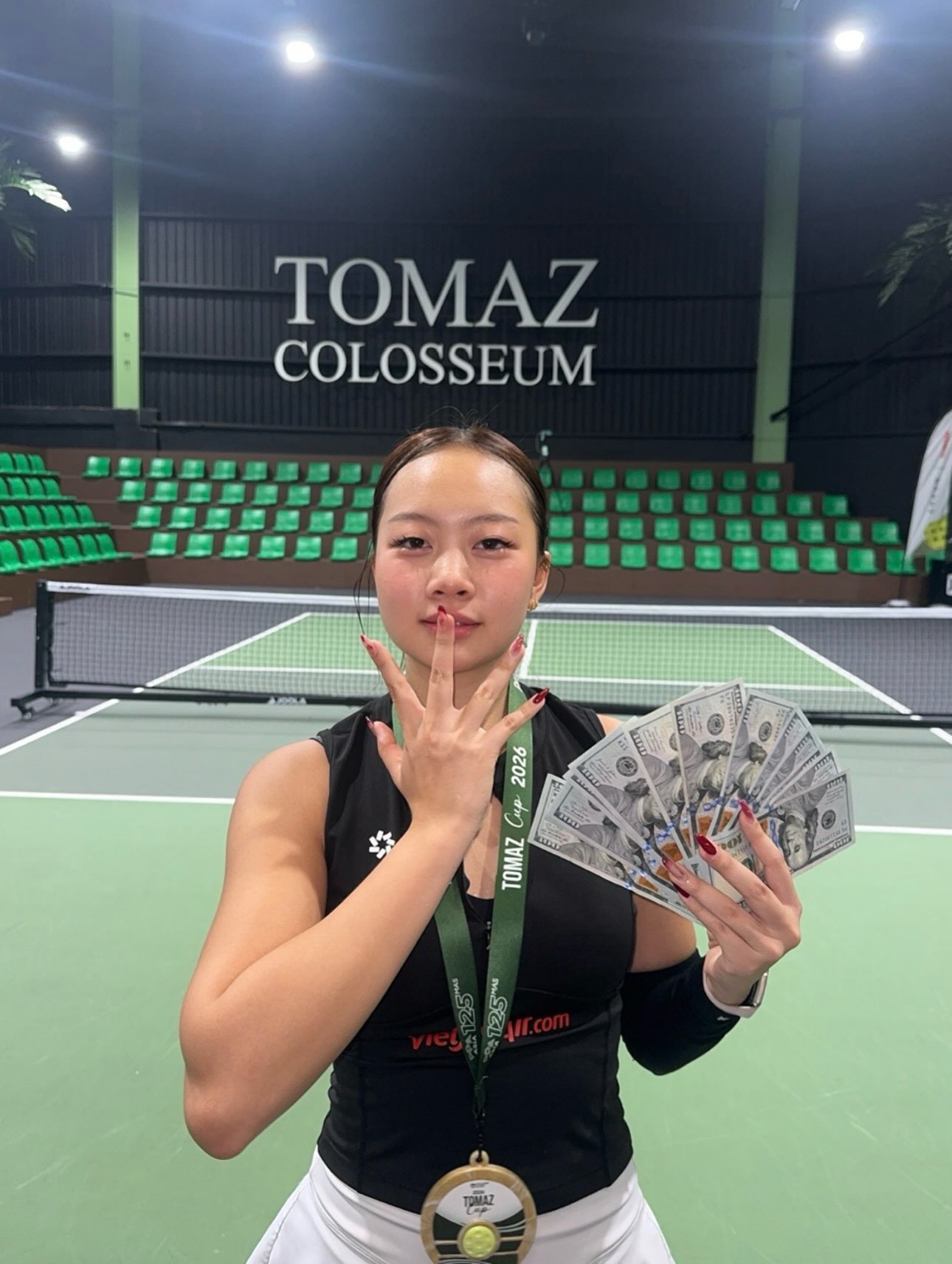 Sophia Tran holds her gold medal in front of the Tomaz Colosseum sign.