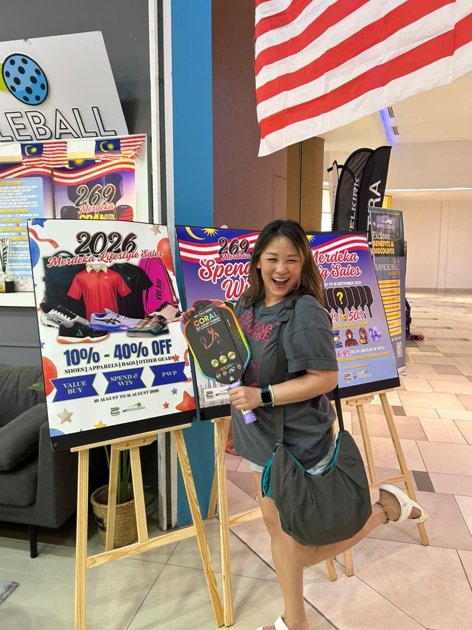A winning MyPickleball customer poses with a Coral all-court paddle in front of the Merdeka sale posters at the Strand Mall outlet.