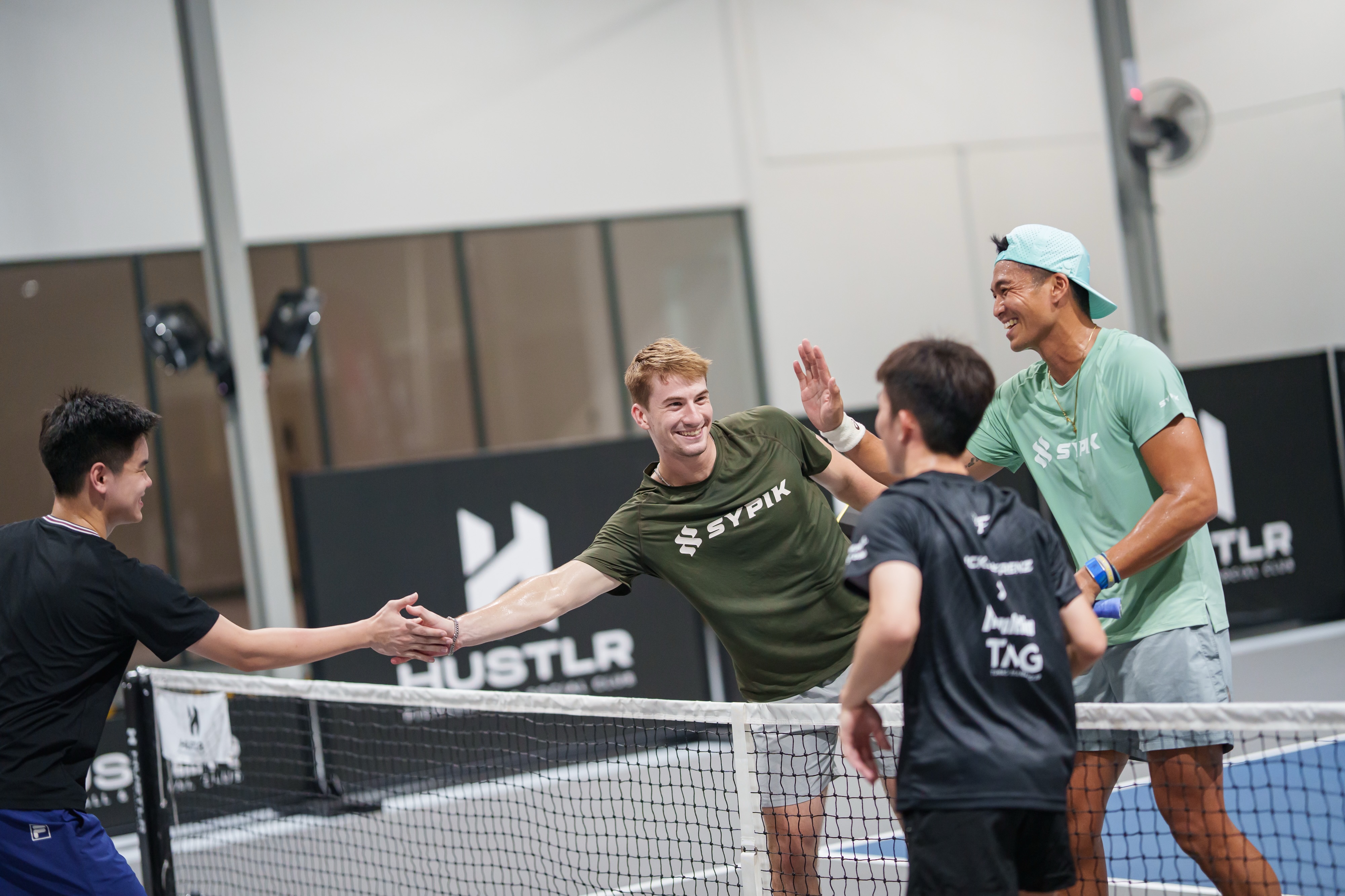 Sypik pro player high-fiving a community member across the net at Hustlr Pickleball and Social Club