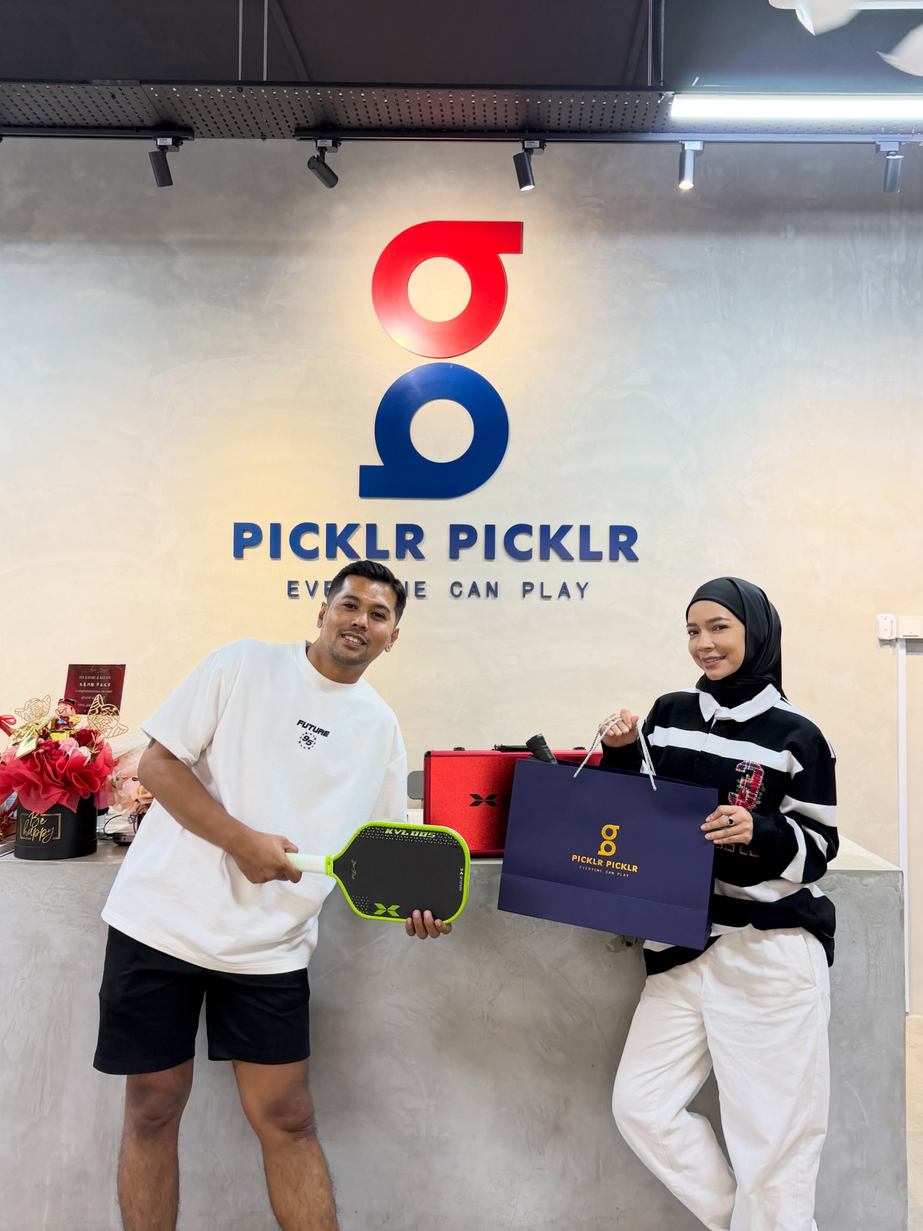 Picklr Picklr staff member presenting actress Noradanish with an Arronax paddle and gift set at the store counter