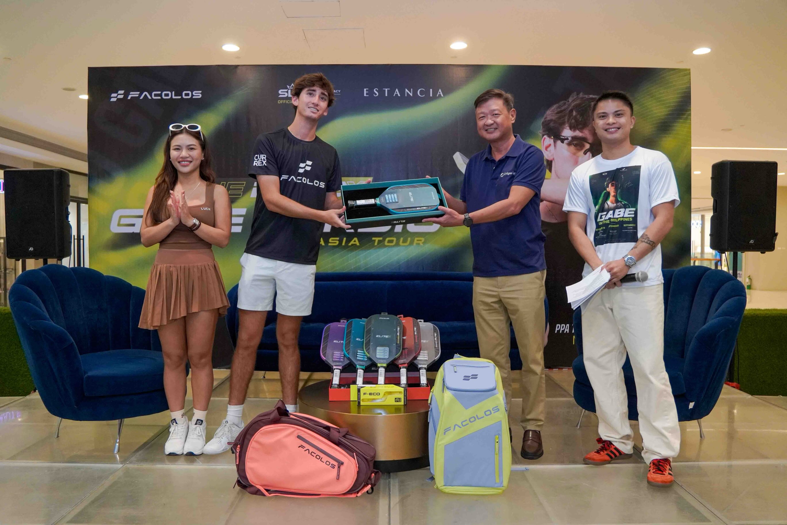 Gabe Tardio hands a boxed EliteX V2 paddle to an Ortigas Land representative on stage at Estancia, with the EliteX V2 colourway lineup and Facolos bags on display