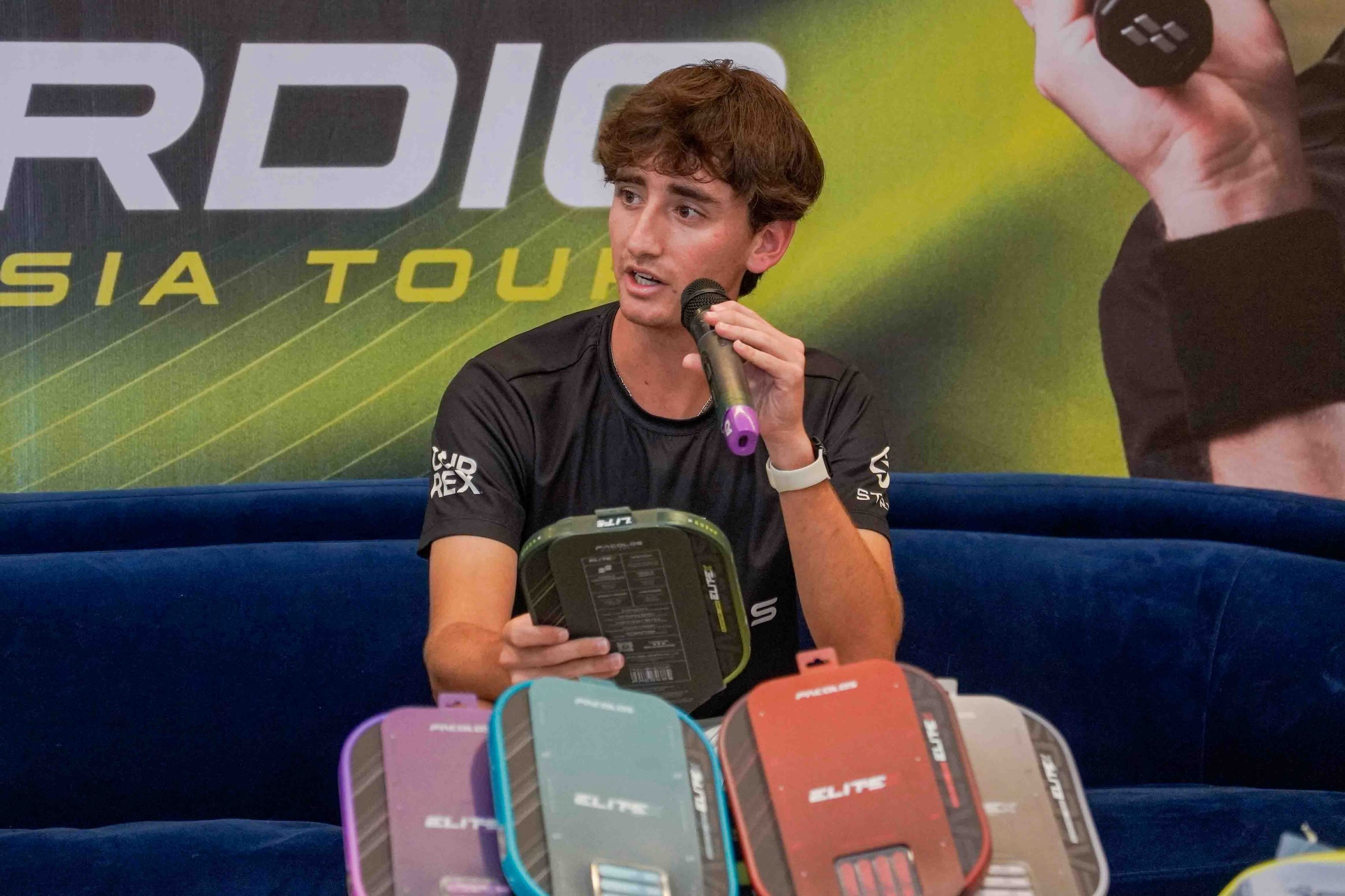 Gabe Tardio holds a microphone and an EliteX V2 spec box on stage in the Philippines