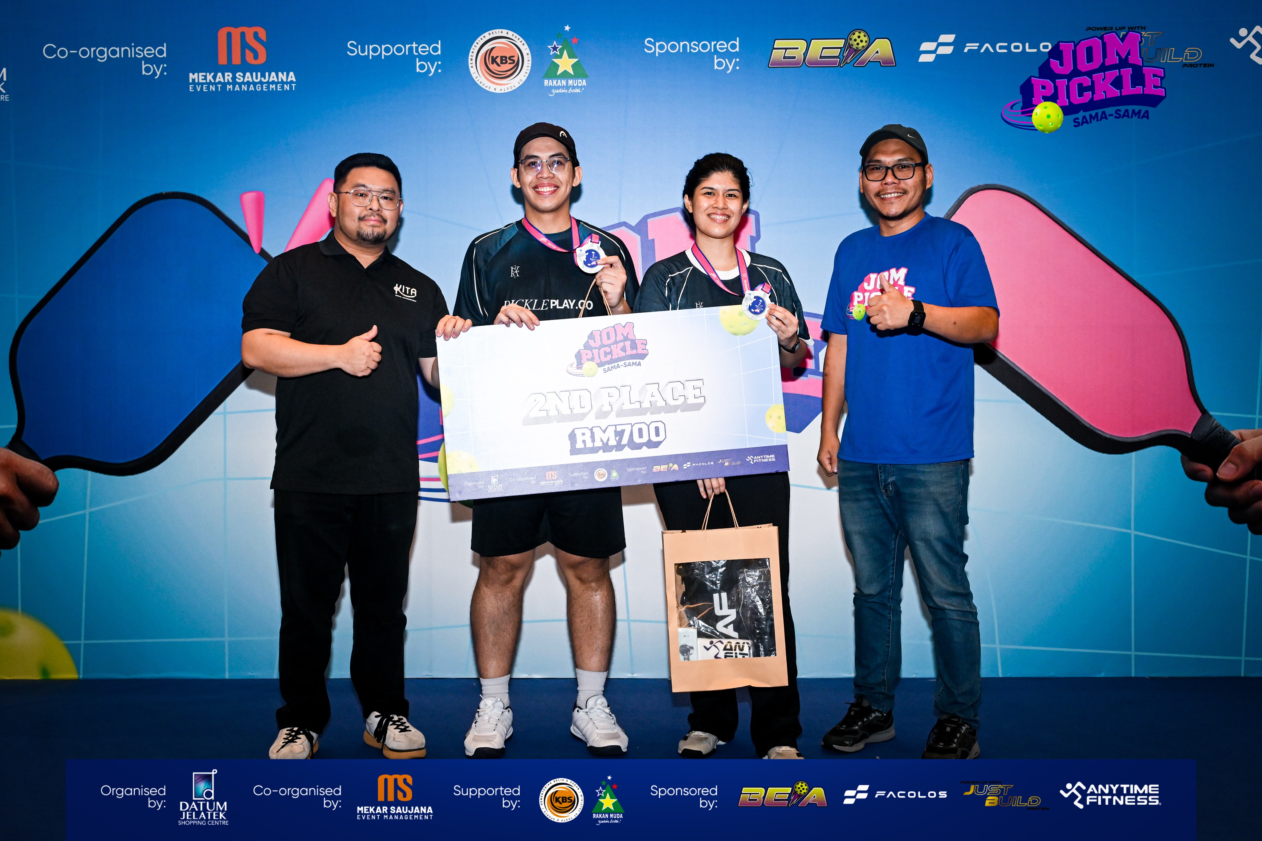 Two PicklePlayCo players with silver medals holding a 2nd place RM700 board