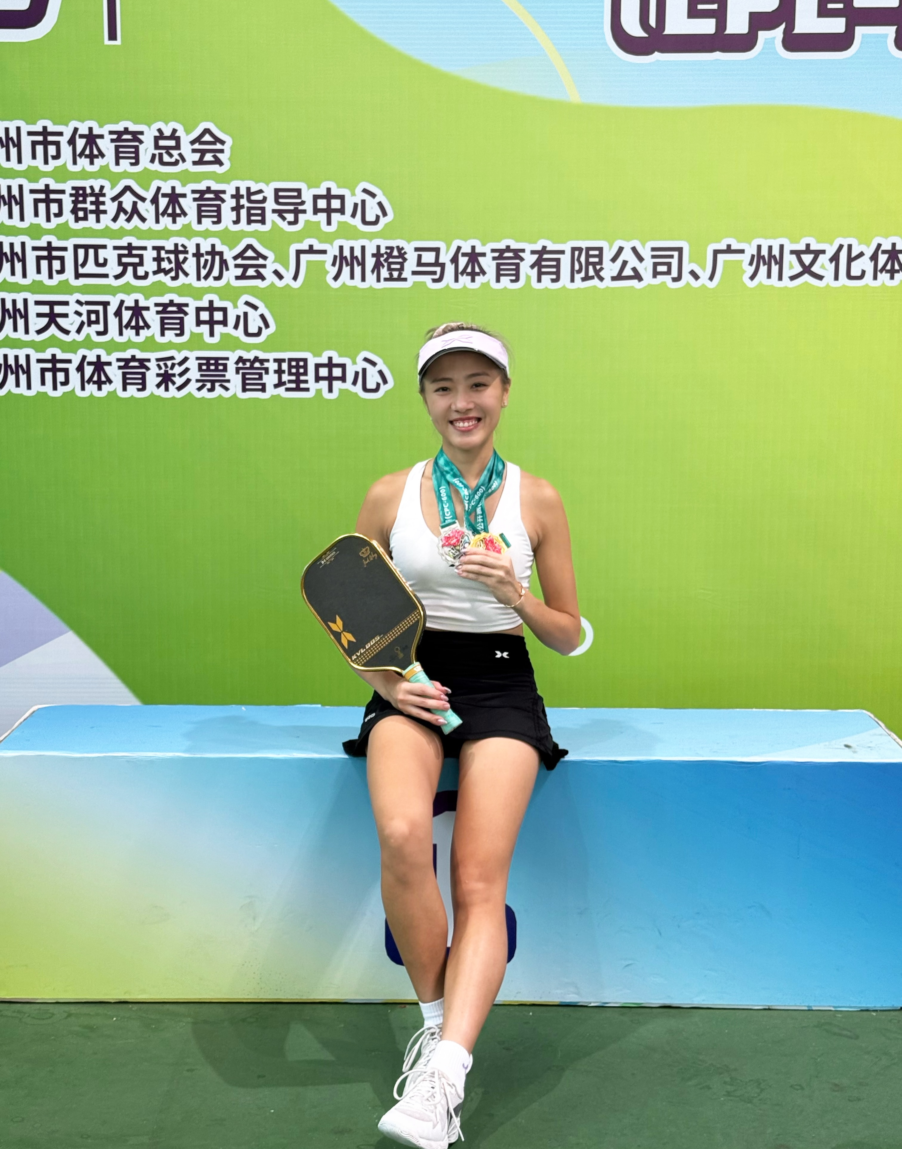 Agnes Fan seated with a medal and paddle in front of the Guangzhou Pickleball Open backdrop