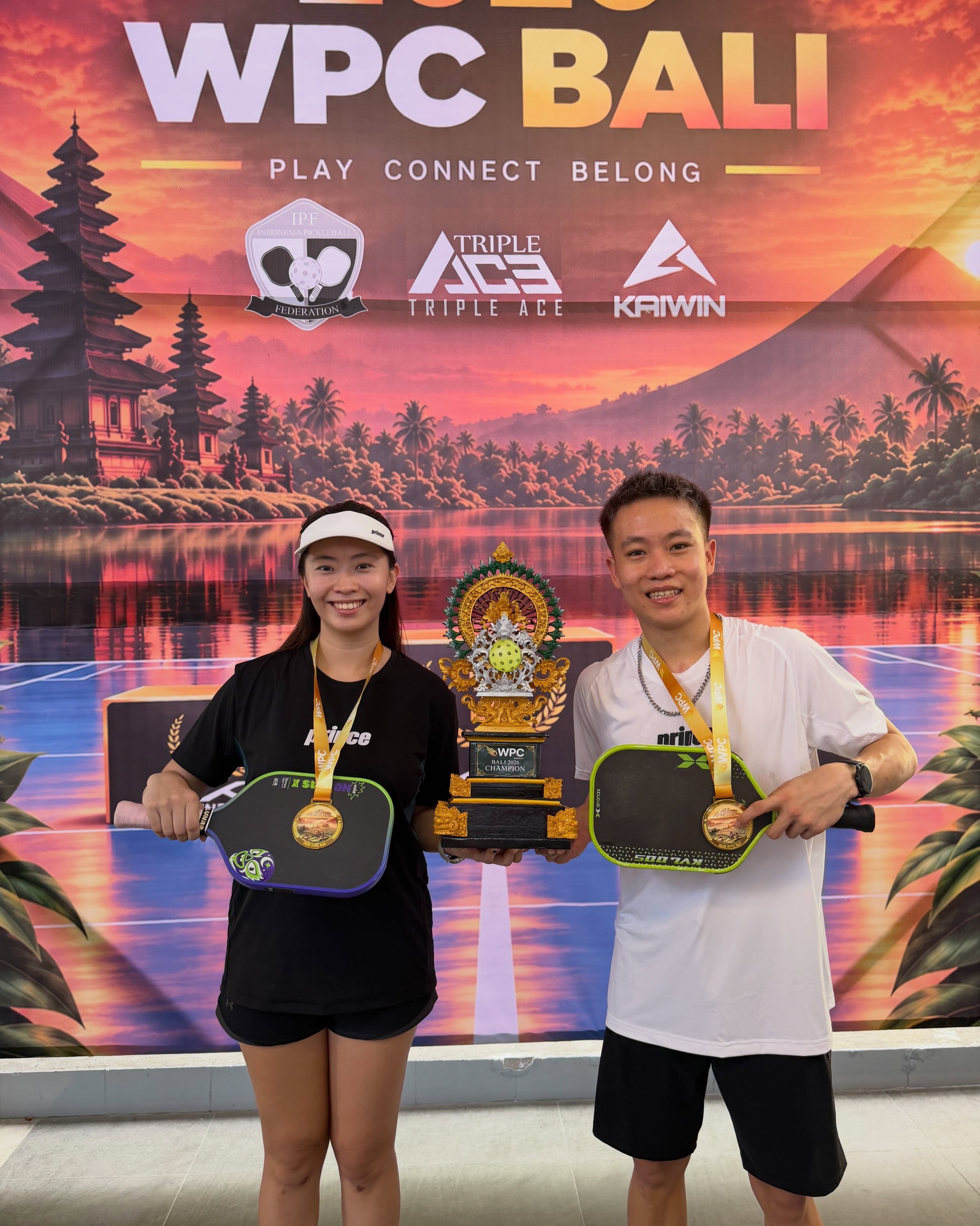 Lagger Chan with a woman, both wearing gold medals, holding the WPC Bali 2026 Champion trophy