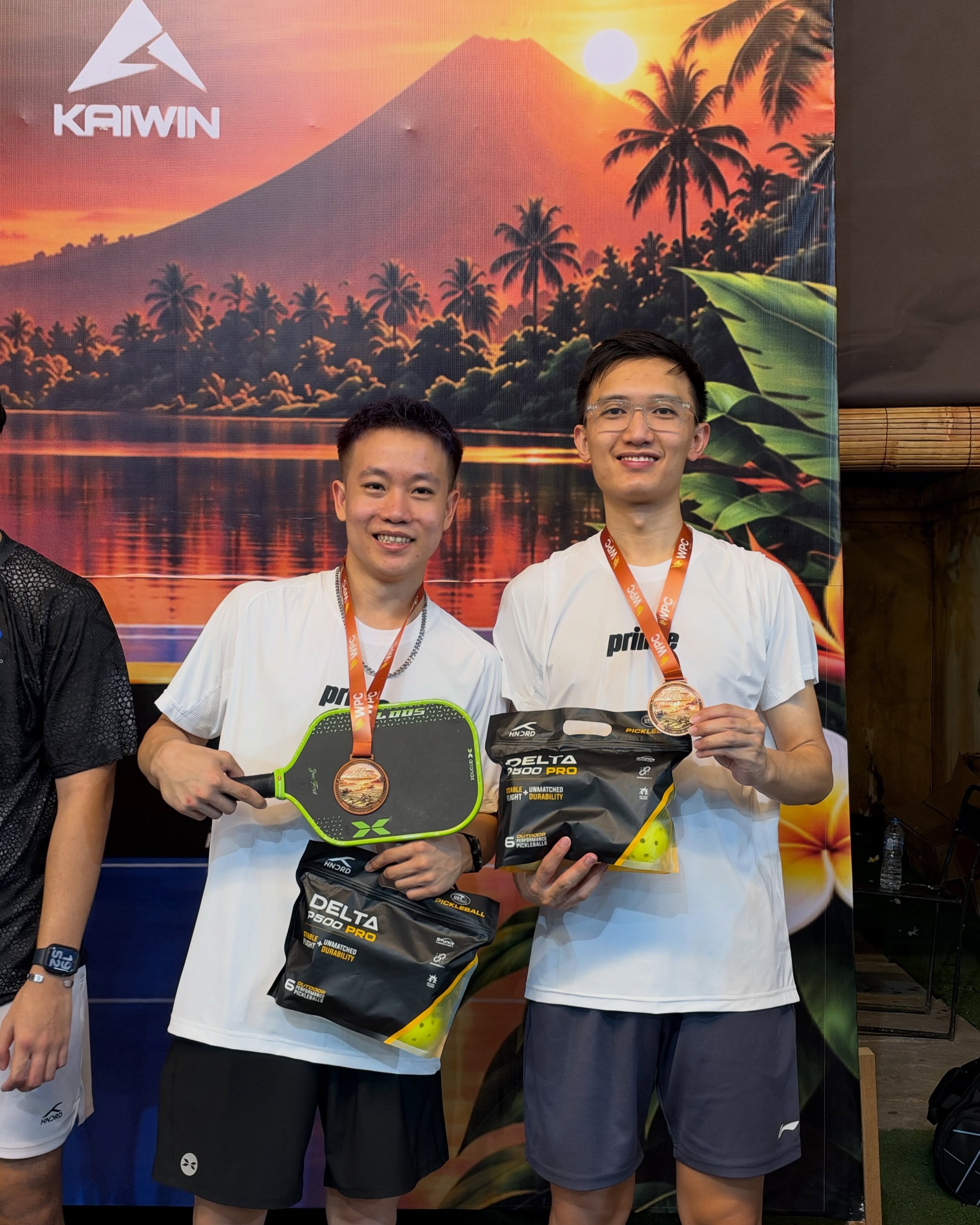 Two men wearing bronze medals holding paddles and ball packs