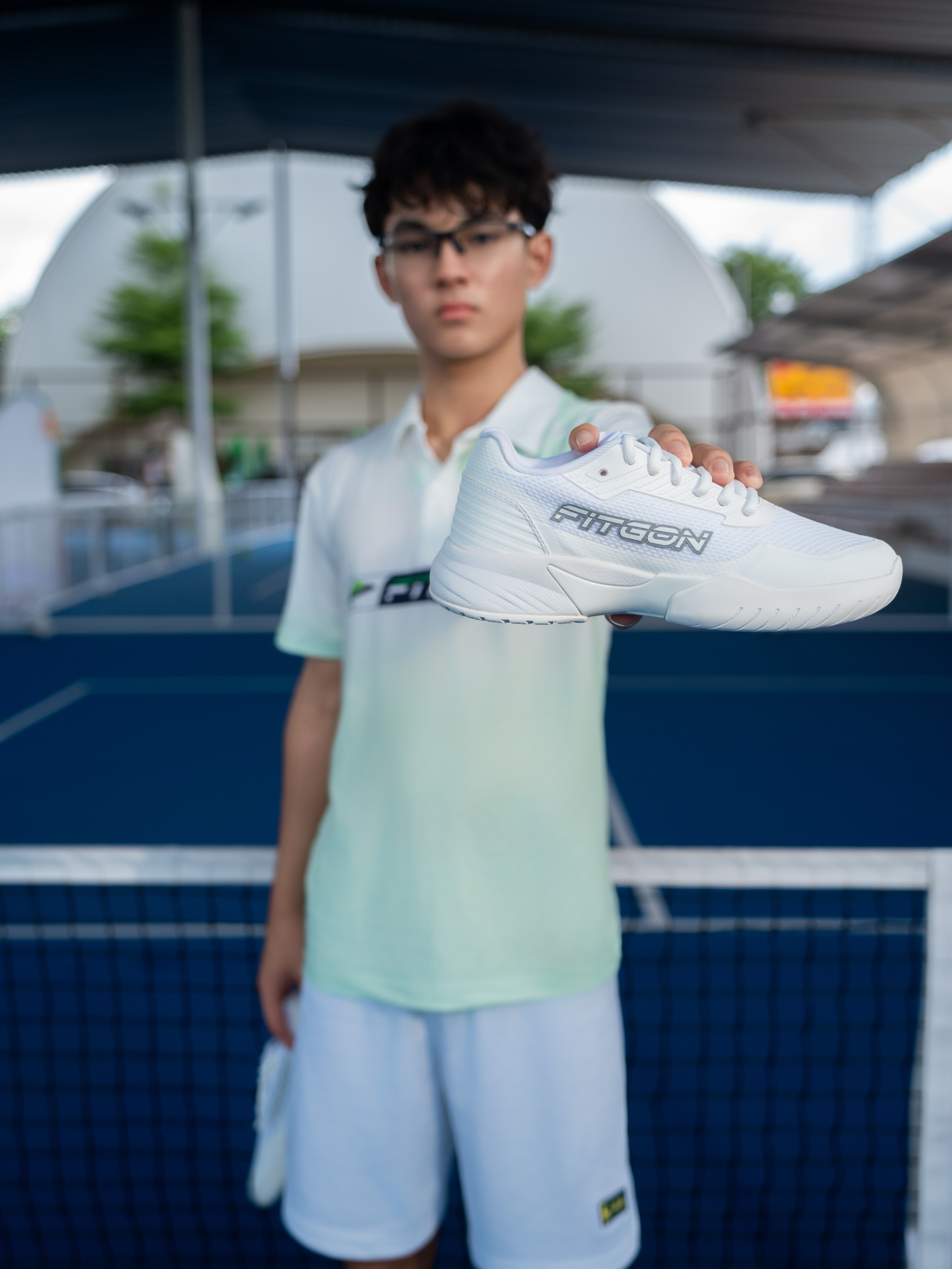 Rex Thais holding a white Fitgon shoe toward the camera on a court