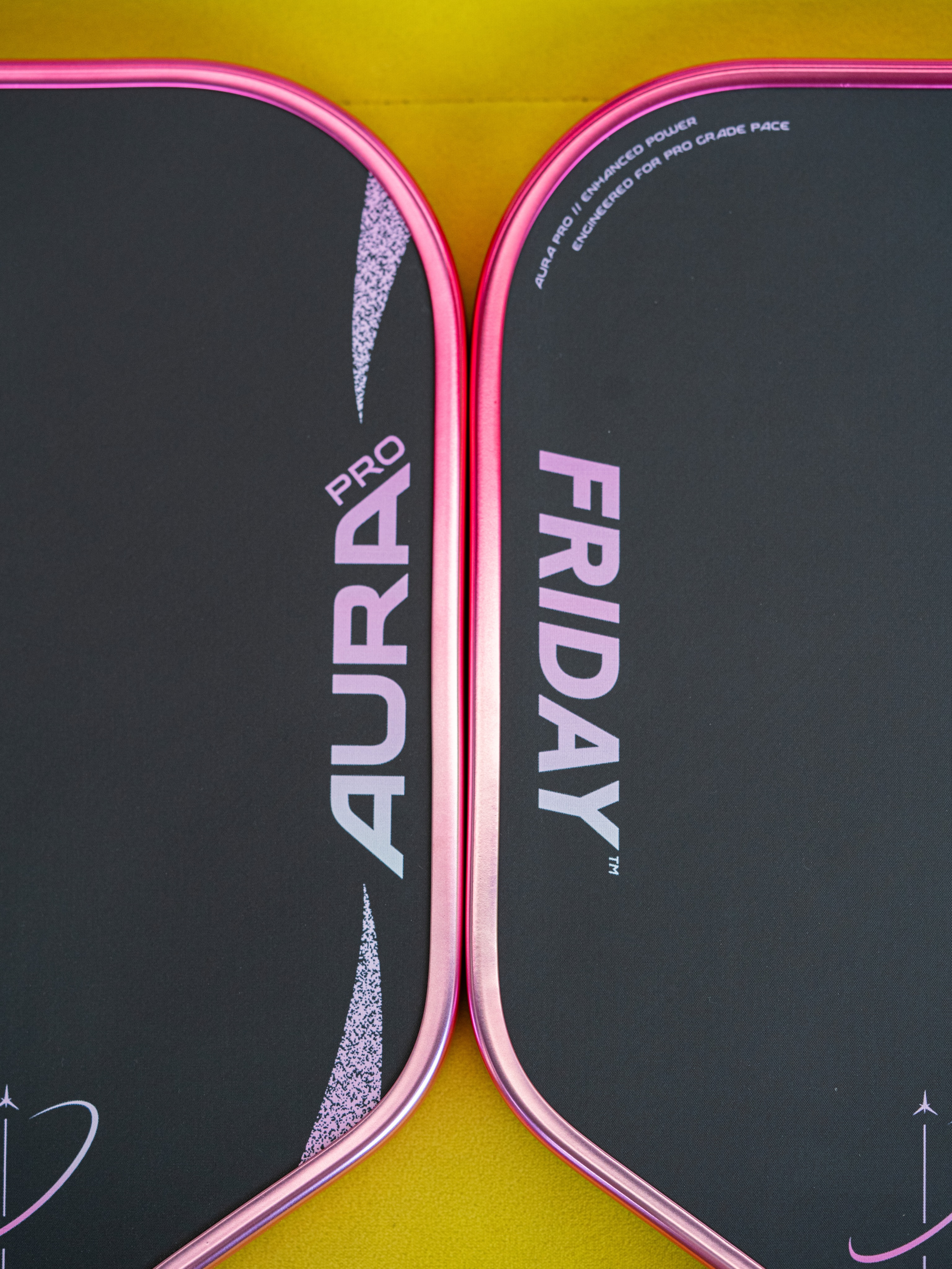Two Friday Aura Pro paddles with pink grips on a yellow surface.