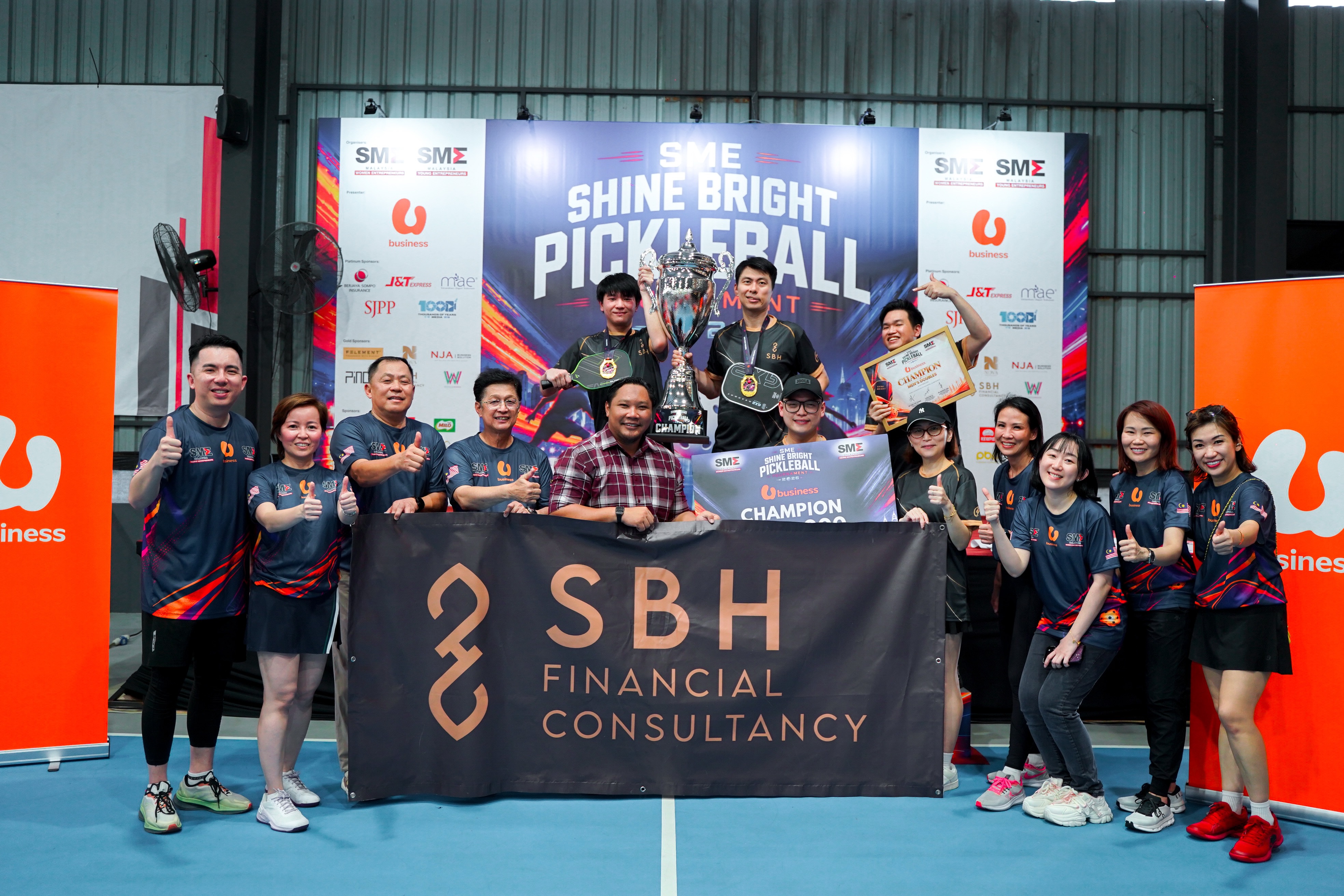 Men's Doubles champions holding the trophy and a Champion Men's Doubles certificate in front of an SBH Financial Consultancy banner