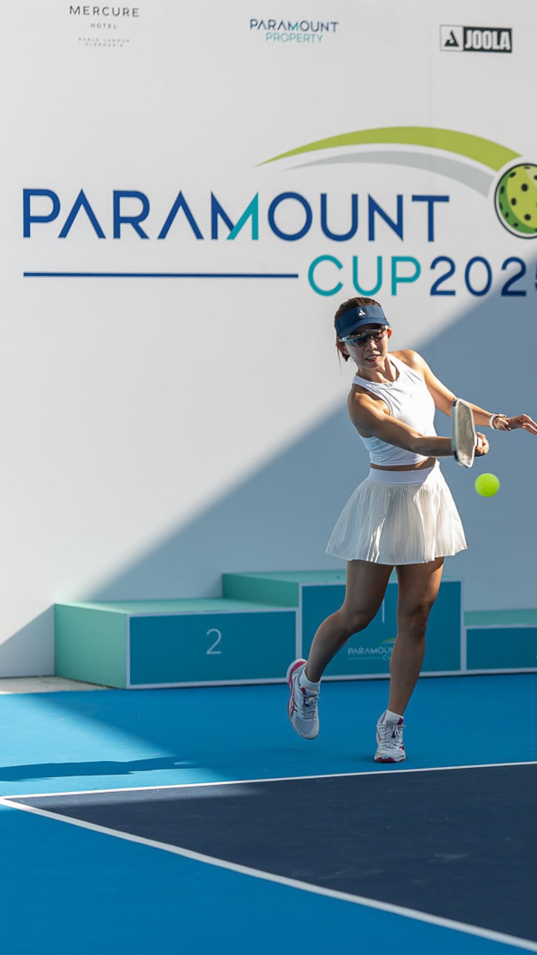 A player hitting a forehand in front of the Paramount Cup backdrop and podium