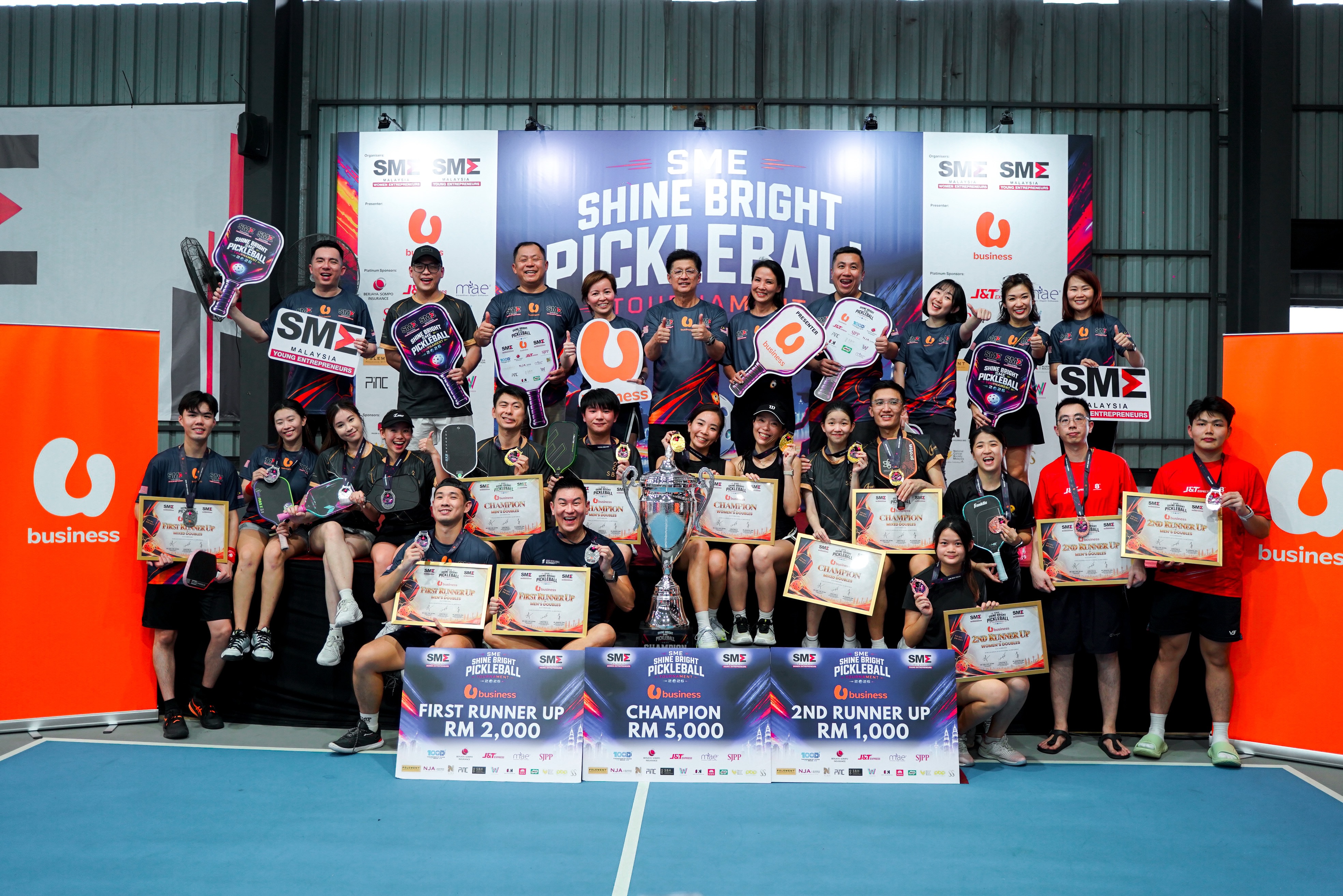 Medallists and organisers on the podium stage with the trophy and the RM5,000, RM2,000 and RM1,000 prize boards at the SME Shine Bright Pickleball Tournament 2026
