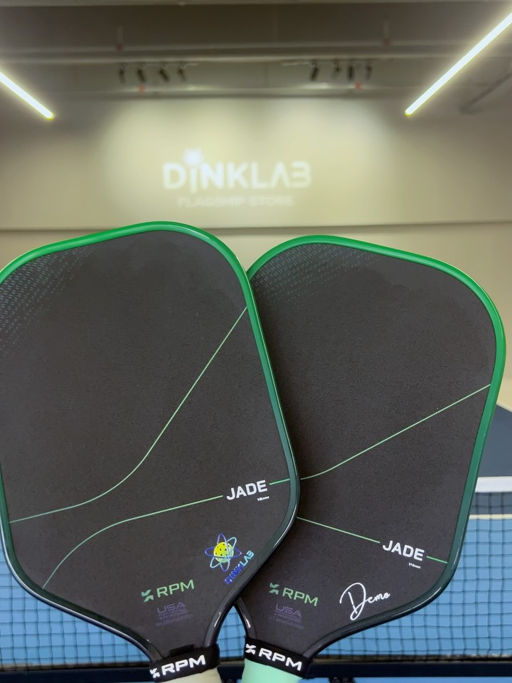 Two RPM Jade paddles held up in front of the DINKLAB Flagship Store sign, one marked Demo