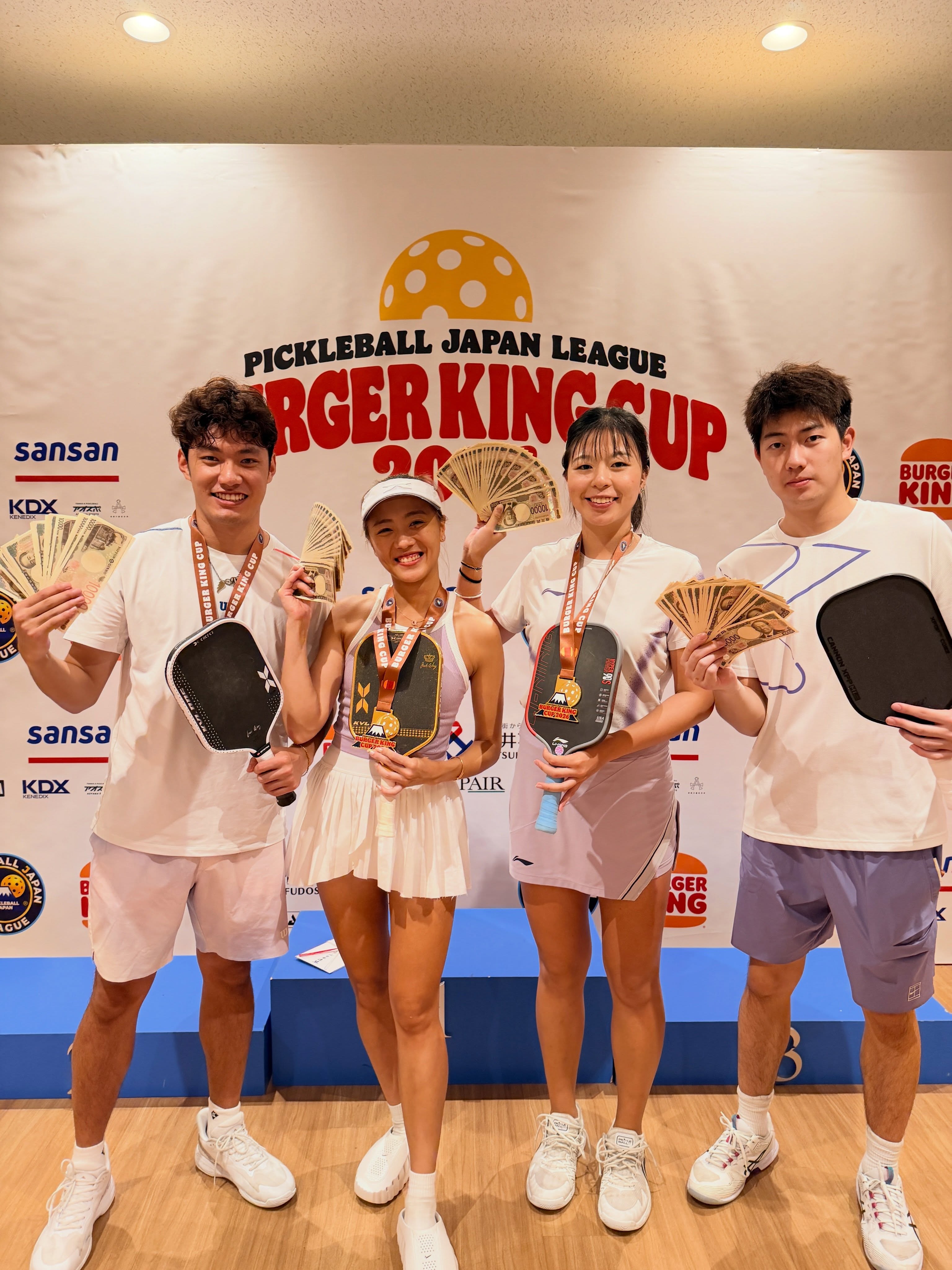 Four players with Burger King Cup medals and yen notes at the Pickleball Japan League Burger King Cup 2026 backdrop