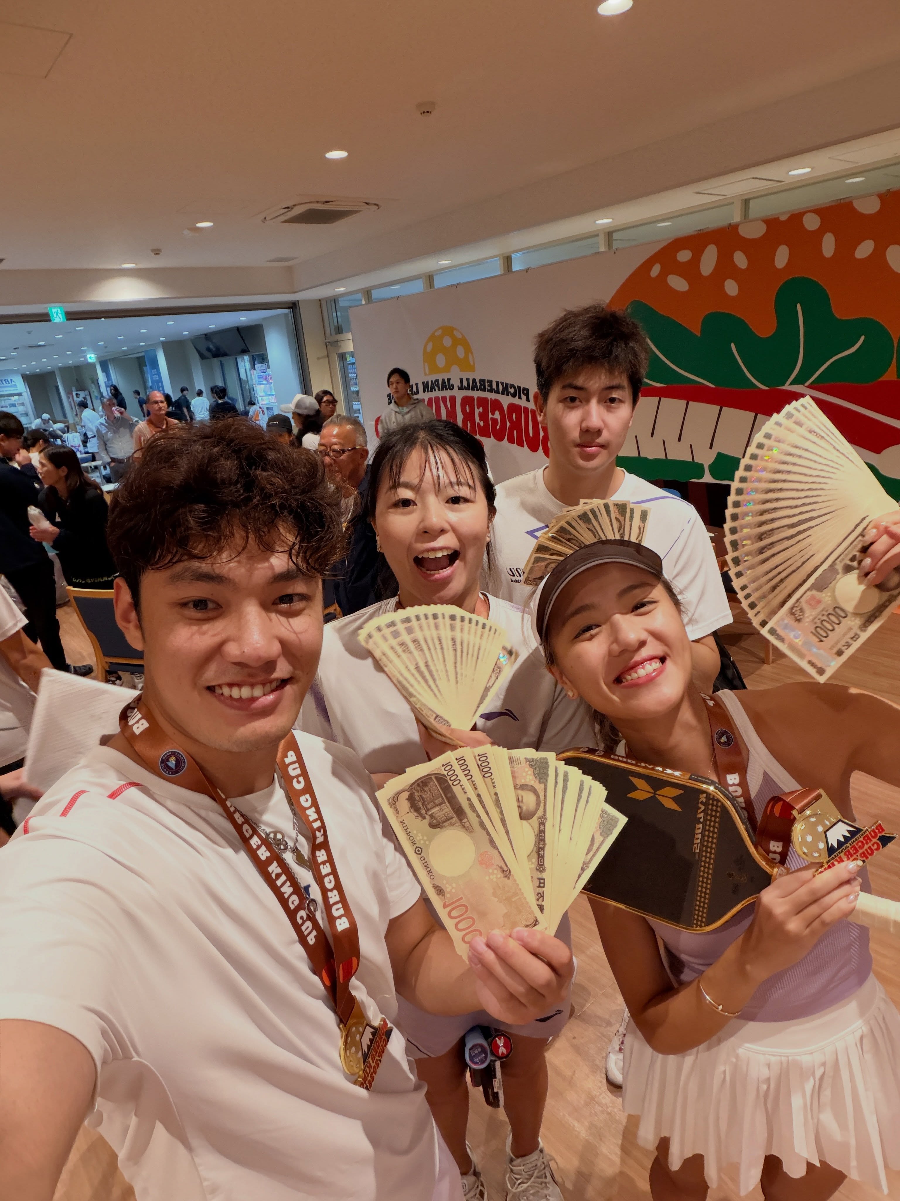 Four players holding fans of yen notes and medals in a venue hall