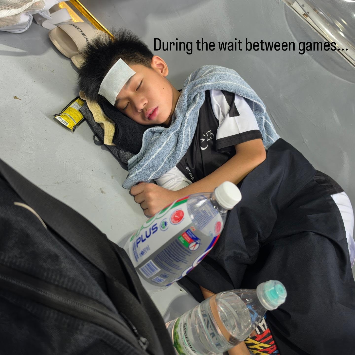 A junior player lying on the floor with a cooling patch on his forehead and a towel, resting between games