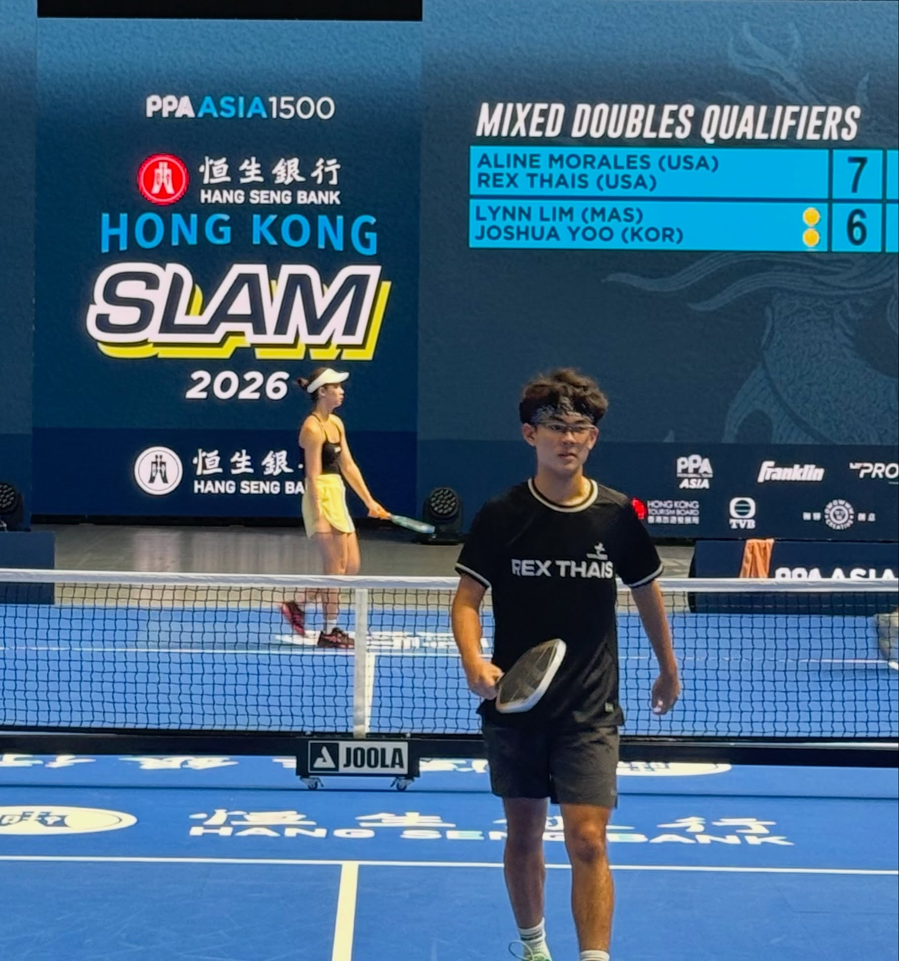 Rex Thais on court in front of a scoreboard reading Mixed Doubles Qualifiers at the Hong Kong Slam