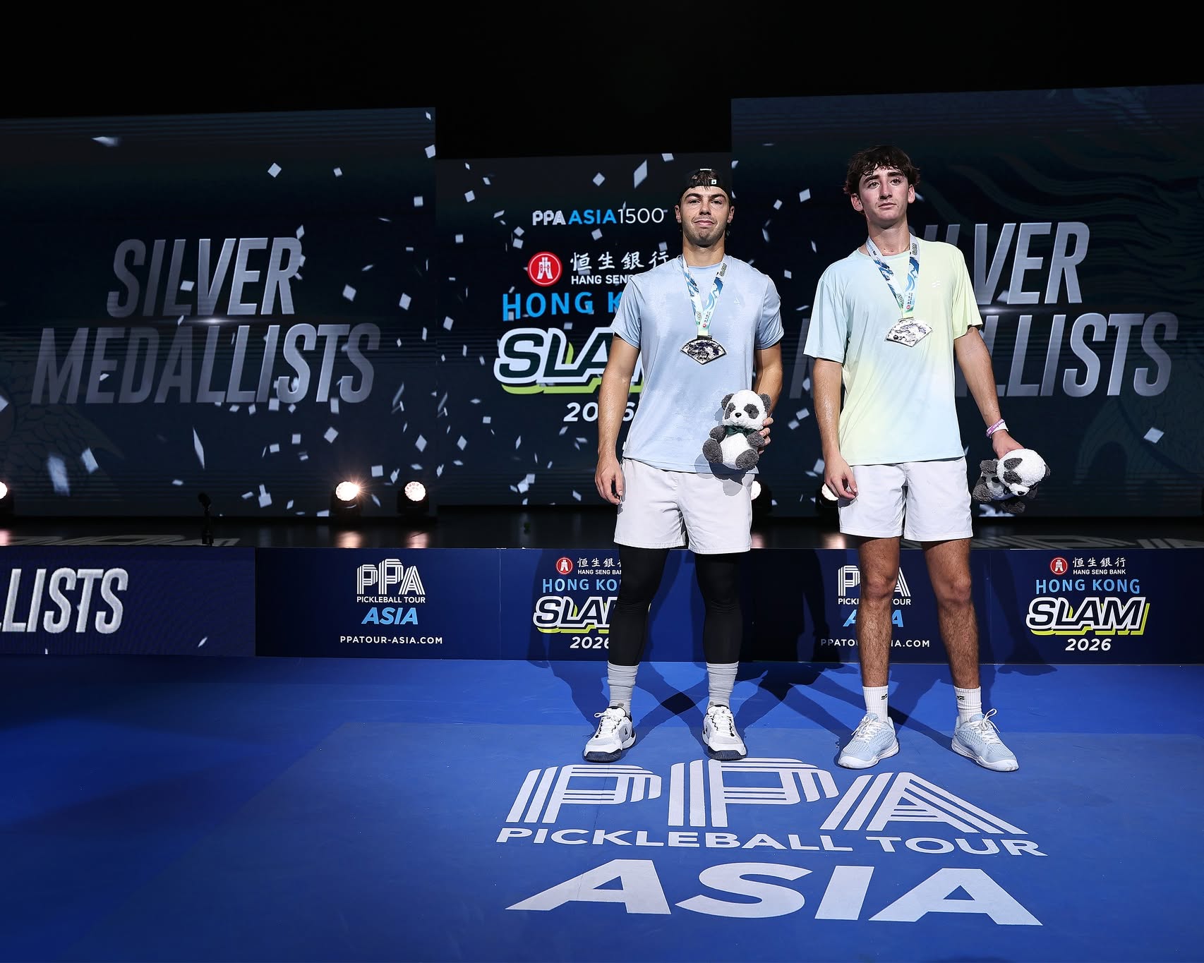 The two silver medalists stand with medals and panda plush toys in front of the Silver Medallists screen at the Hong Kong Slam