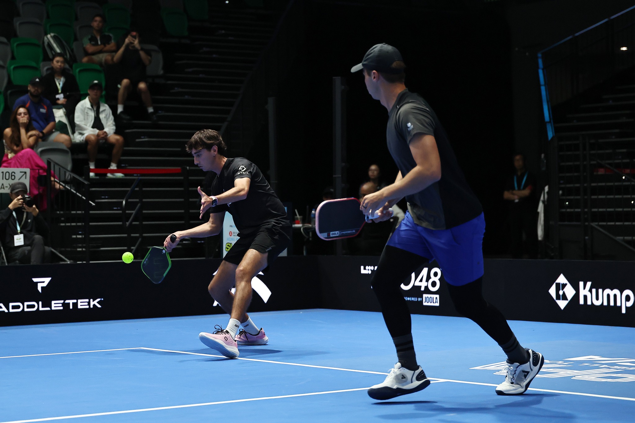 A player in black reaches low for a ball during a doubles match at the Hong Kong Slam