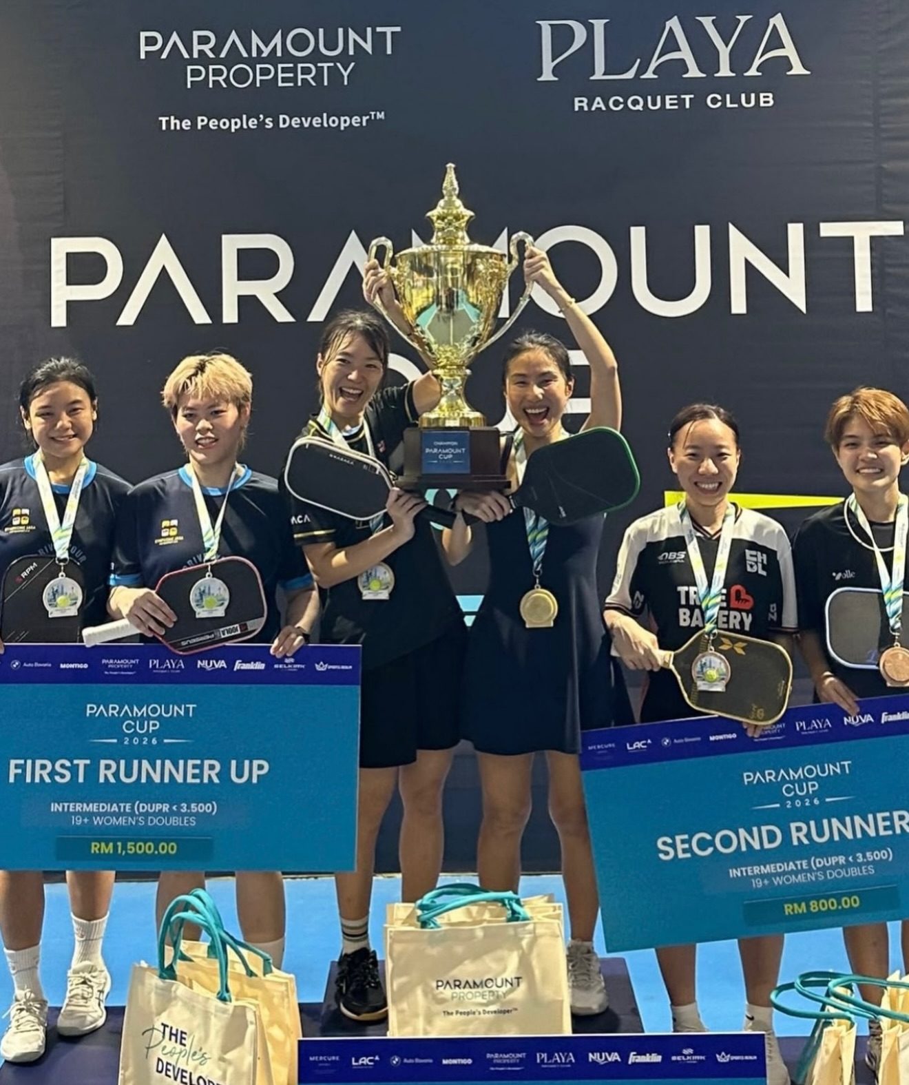 The Intermediate 19+ Women's Doubles podium at Paramount Cup 2026, with the champions lifting the trophy between the first and second runner-up teams